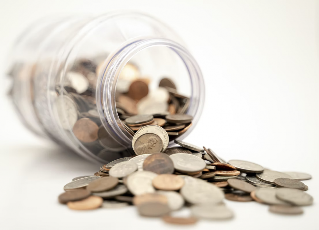 Image of a jar full of spare change spilled over against a white background.