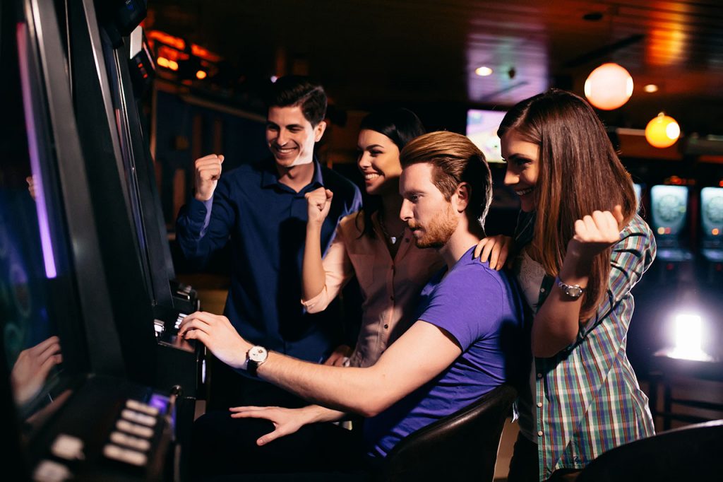  Young Slots Player at a Machine with Friends Around
